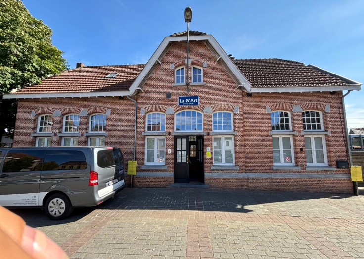 Vooraanzicht van een roodstenen gebouw met een bord "La G'Art" en een geparkeerde grijze bestelwagen. (vergroot foto)